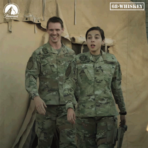 two people in army uniforms standing in front of a large sheet