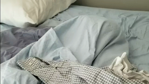 an unmade bed with a plaid shirt and sheets on it
