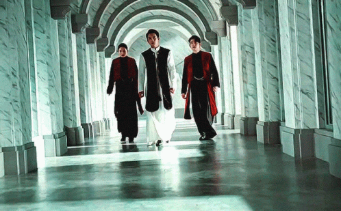 three men wearing blue and white walking down a hall with arches