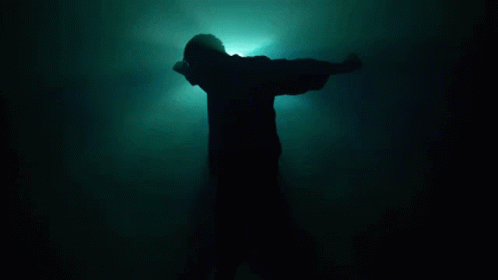 a silhouette of a person with arms outstretched in front of a dark room