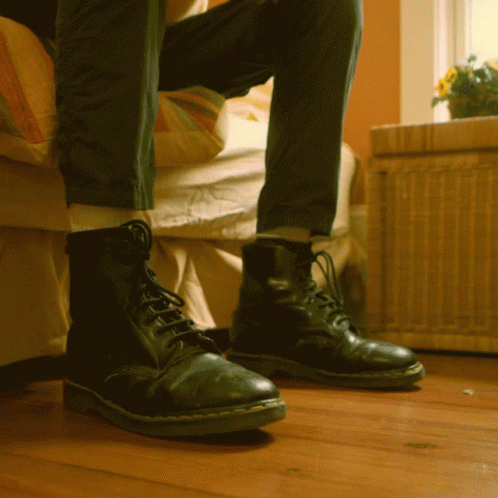 a person wearing leather boots, standing near a bed