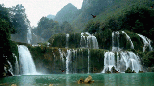 a waterfall in the distance with birds flying