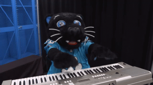a black cat mascot standing with its hands out next to a keyboard