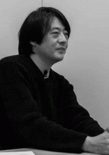 a man with black hair sitting at a table looking to the side