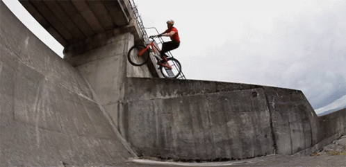 a man on a bicycle riding up the side of a cement ramp