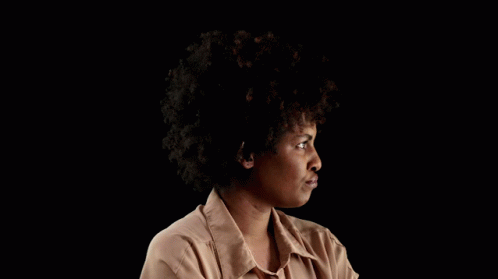 a woman with an afro sitting in front of a dark background
