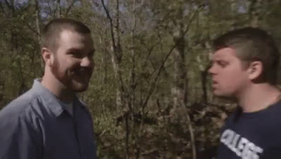 two men standing next to each other outside in the woods