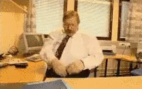 a man in an office setting is seen from the reflection of a computer screen