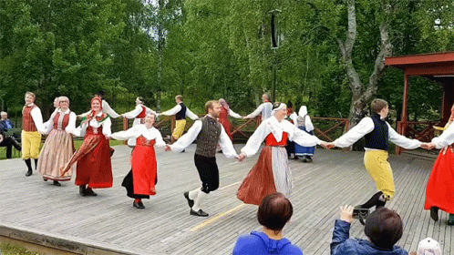 several people dance on a deck in front of some green trees