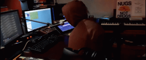 a man wearing a hood is sitting at a desk with multiple computers
