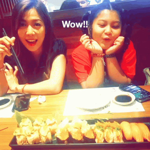 two asian women are sitting at a table with plates of sushi