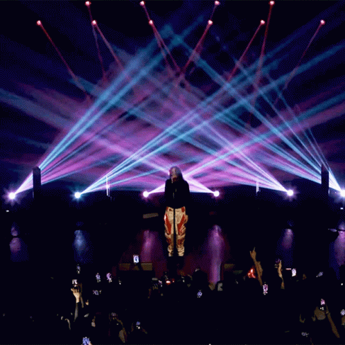 people standing on stage with their arms spread out and spotlights coming from their backs