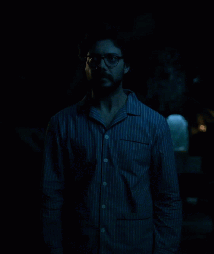 a man standing in the dark wearing glasses
