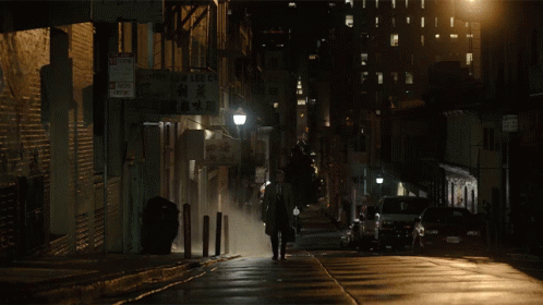 man in black walking alone on wet city street