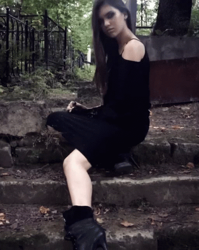 a woman in a black dress is sitting on a set of steps