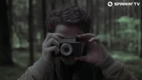 a boy holds a camera and takes a po in the woods