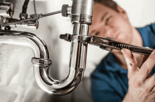 an industrial plumter has his wrench hooked to a pipe that is in the sink
