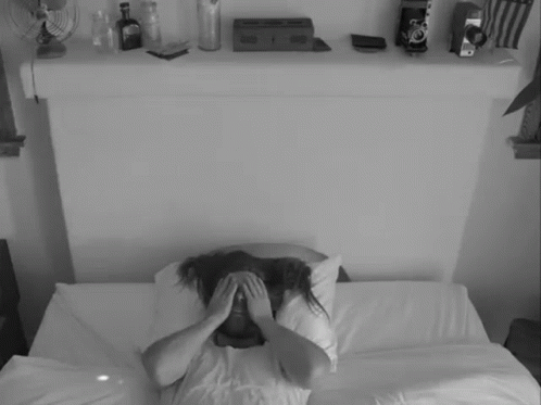 a woman sitting on a bed covering her eyes