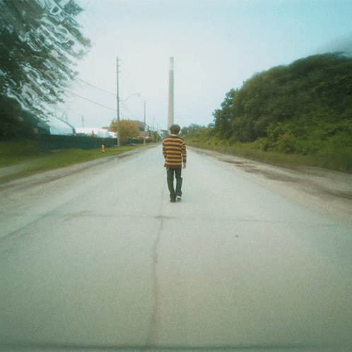 man walking down empty road, on a skateboard