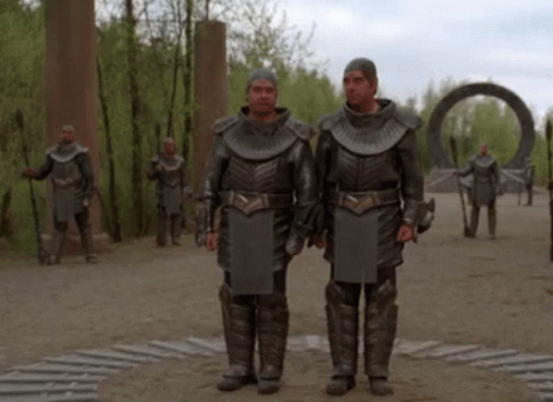 two men in armor stand in front of a group of other men