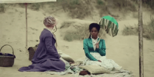 two women sitting under an umbrella in the sand