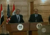 three people standing behind blue podiums with flags in the background