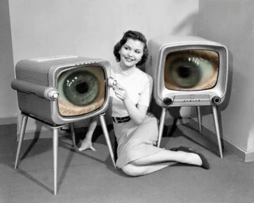 a woman is lying on the floor next to two televisions with large eyes on them
