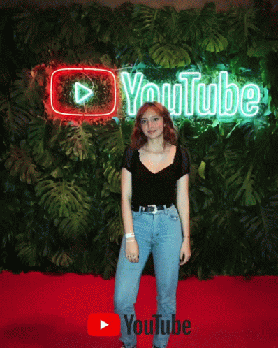 a woman standing next to a green wall with a large neon sign above her