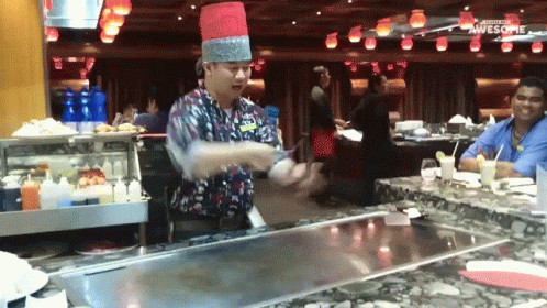 a man wearing a hat and making soing with white plates in a restaurant