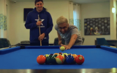two men stand around the pool table with balls