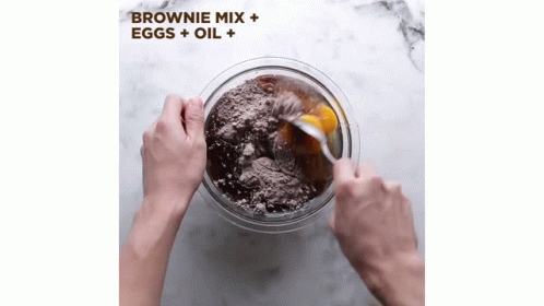 a hand wearing blue gloves picks up a bowl of flour from an advertit for brownie mix
