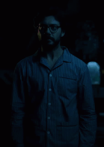 a man standing in the dark wearing glasses