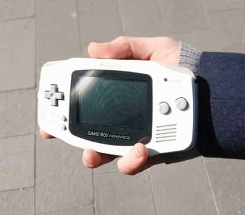 an older man with blue gloves holds up a small game boy