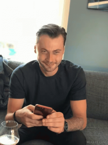 a man is smiling at the camera while looking at his cell phone