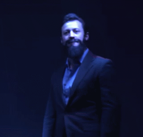 man with beard and tan shirt standing in dark room