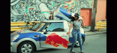 a girl standing on the back end of a small car in front of graffiti
