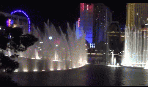 several lit up fountains in front of city buildings