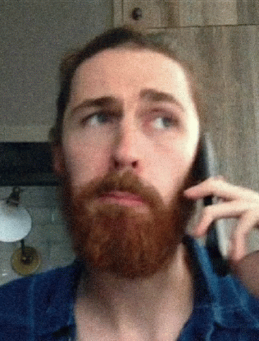 a bearded man standing in front of a mirror talking on his cell phone