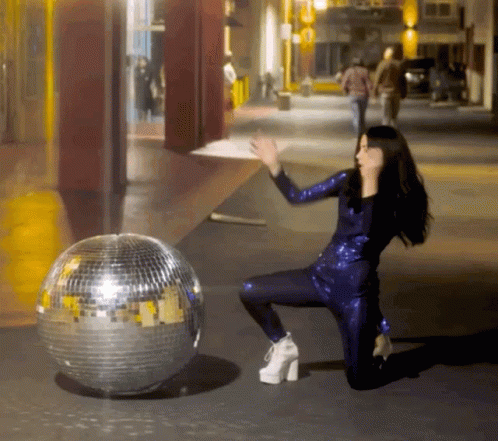 a woman sitting next to a disco ball in the middle of a street