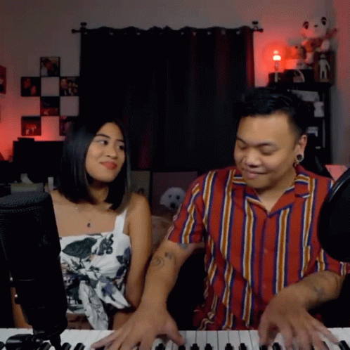 a man sitting behind a woman playing piano together