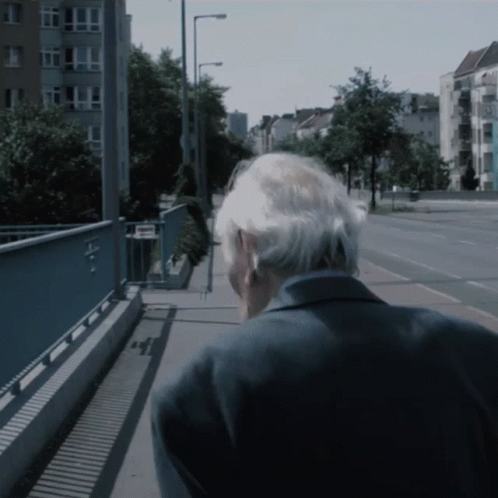 an older man wearing glasses walks down the sidewalk
