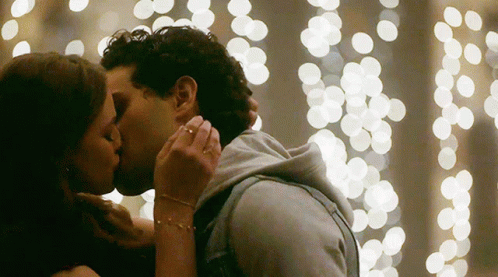 a man and woman kiss in front of a light - filled backdrop