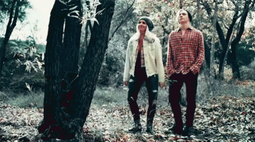 two young men stand in the woods together