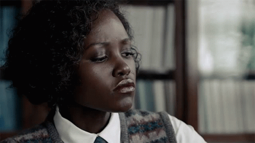 a dark skinned girl wearing a tie and vest looks off to the side
