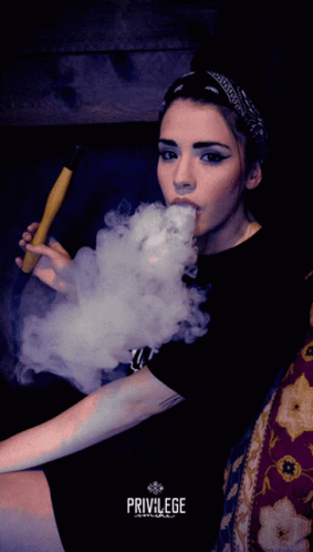 a woman sitting on a couch smoking soing and holding an electronic cigarette