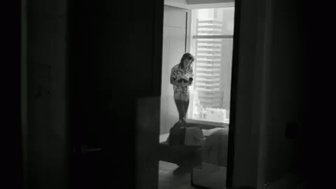 a young woman stands at the window in a dark room
