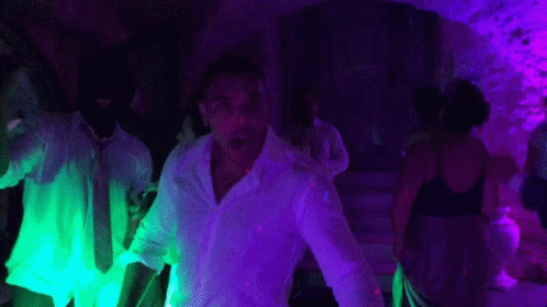 people in white clothes dance around a neon light