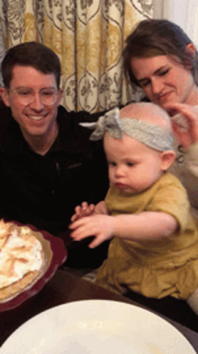 three adults sit and look at a small child sitting in front of a cake
