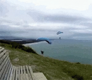 a person with a parasail is flying near a bench