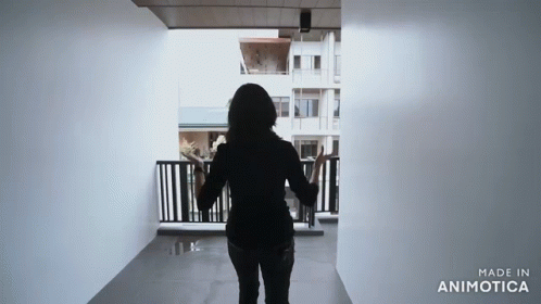 the silhouette of a woman in a black top and black pants in an open hallway with an entrance railing